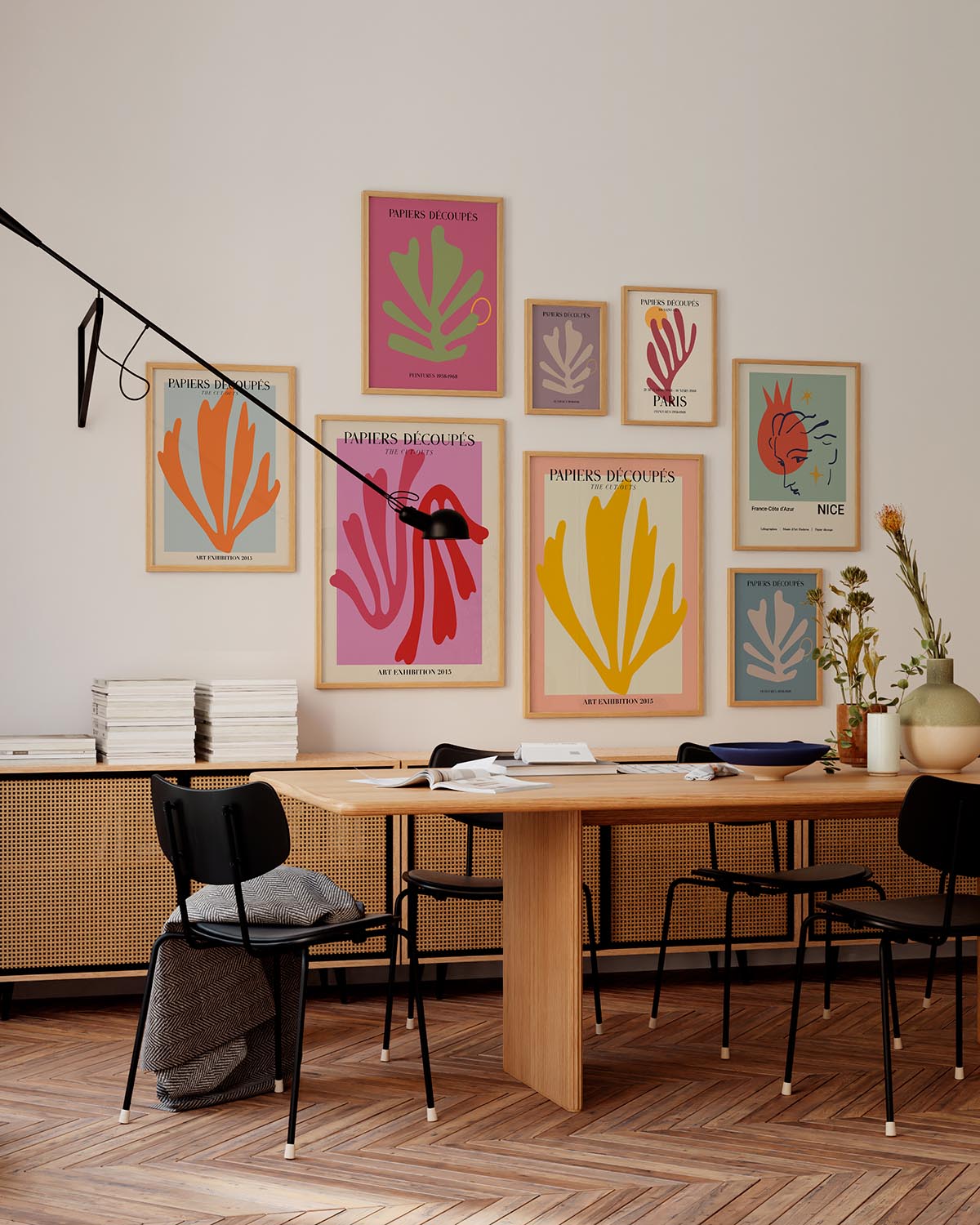 木製のデスク、黒い椅子、ミッドセンチュリーのサイドボードが置かれたモダンなオフィススペースに、マティスにインスパイアされたさまざまな色の「Papiers Découpés」ポスター（gallery wall ）が飾られたインテリアデザイン。