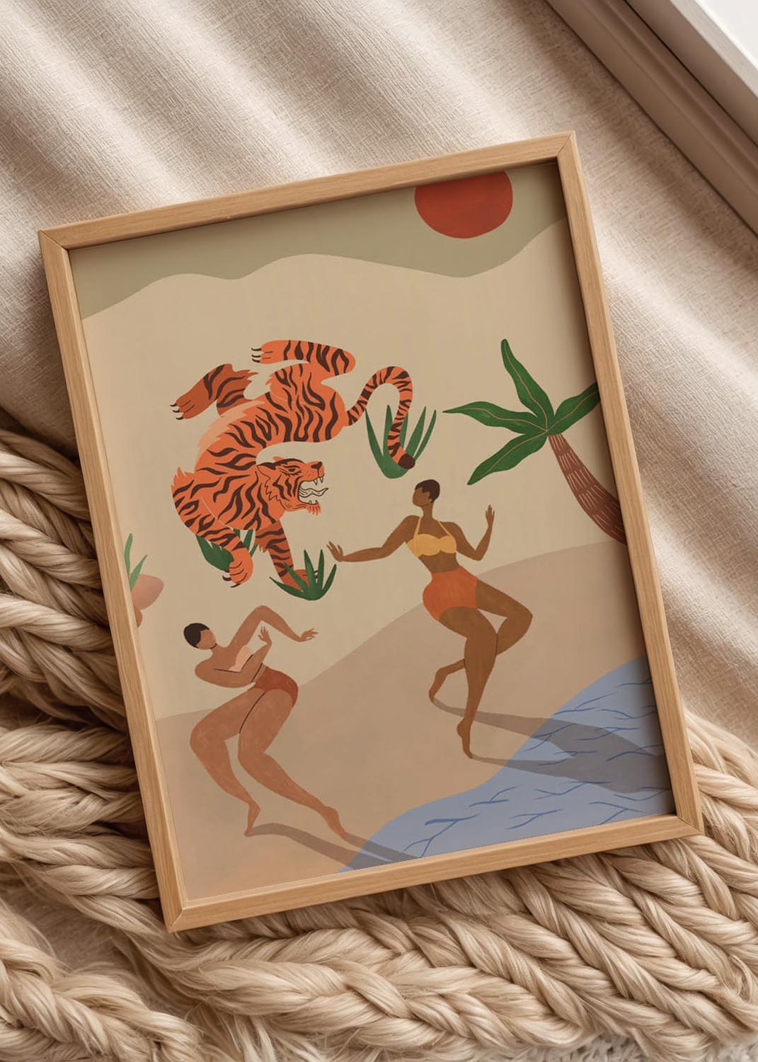 Illustration "Dancing Tigers" by Arty Guava, showing two women in swimwear dancing joyfully on a sandy beach while a large tiger leaps playfully in the air above them, framed by a palm tree and a red sun.