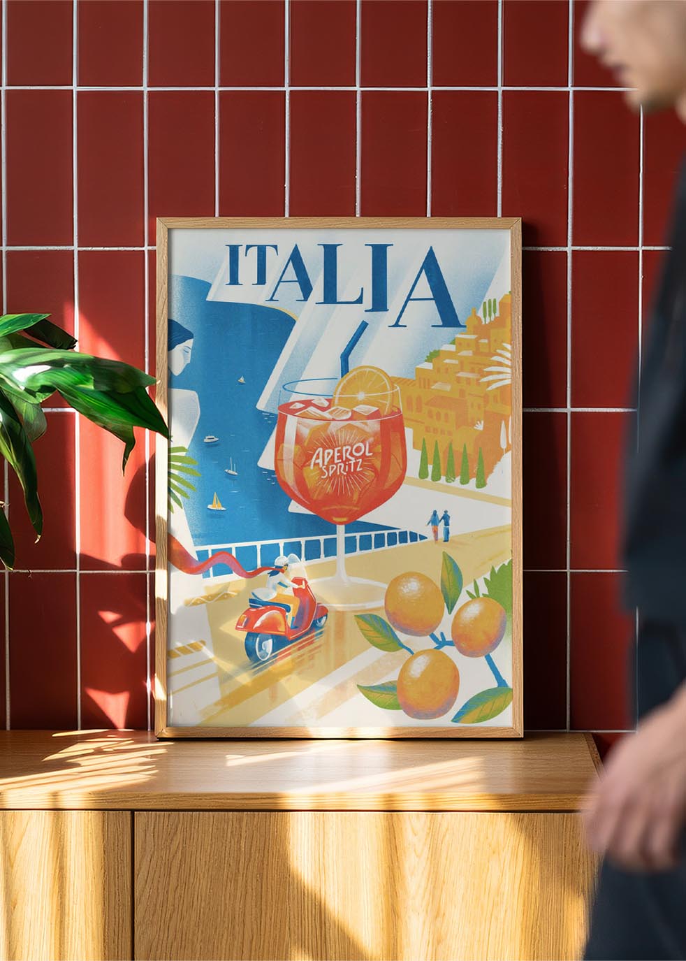 Colorful retro-style poster of an Aperol Spritz glass set against an Italian coastal backdrop, with a couple on a Vespa, citrus trees, and seaside cliffs.