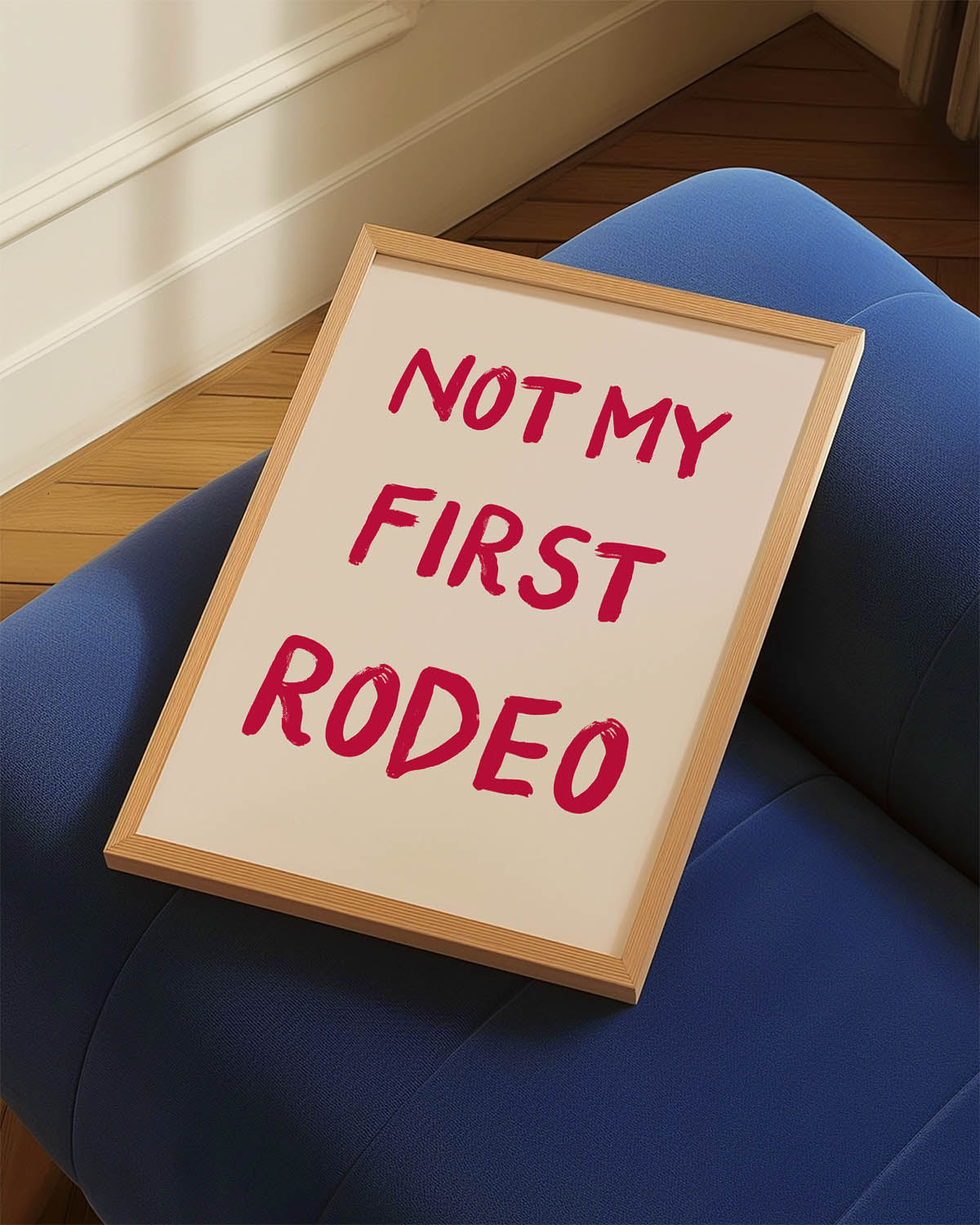A trendy poster with the phrase "NOT MY FIRST RODEO" in bold red brush script font on a pastel pink background, conveying a sense of humor and confidence