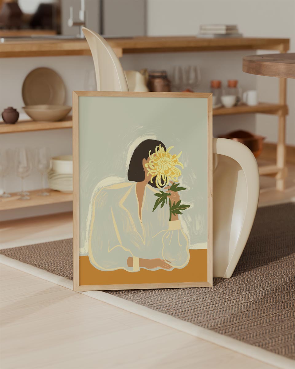 Minimalist illustration titled The Chrysanthemum by Arty Guava, featuring a faceless woman with dark hair holding a large yellow chrysanthemum in front of her face, set against a muted sage background.