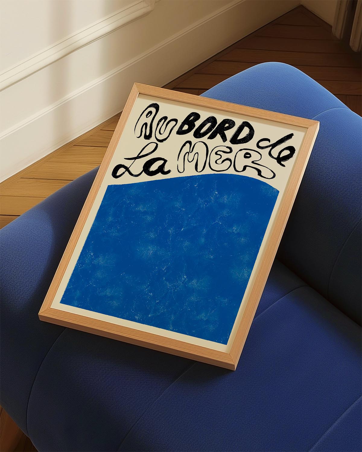 Artistic poster with the French phrase 'Au bord de la mer' in bold black script at the top, over a textured deep blue background that fills the lower section, evoking the peacefulness of the ocean."