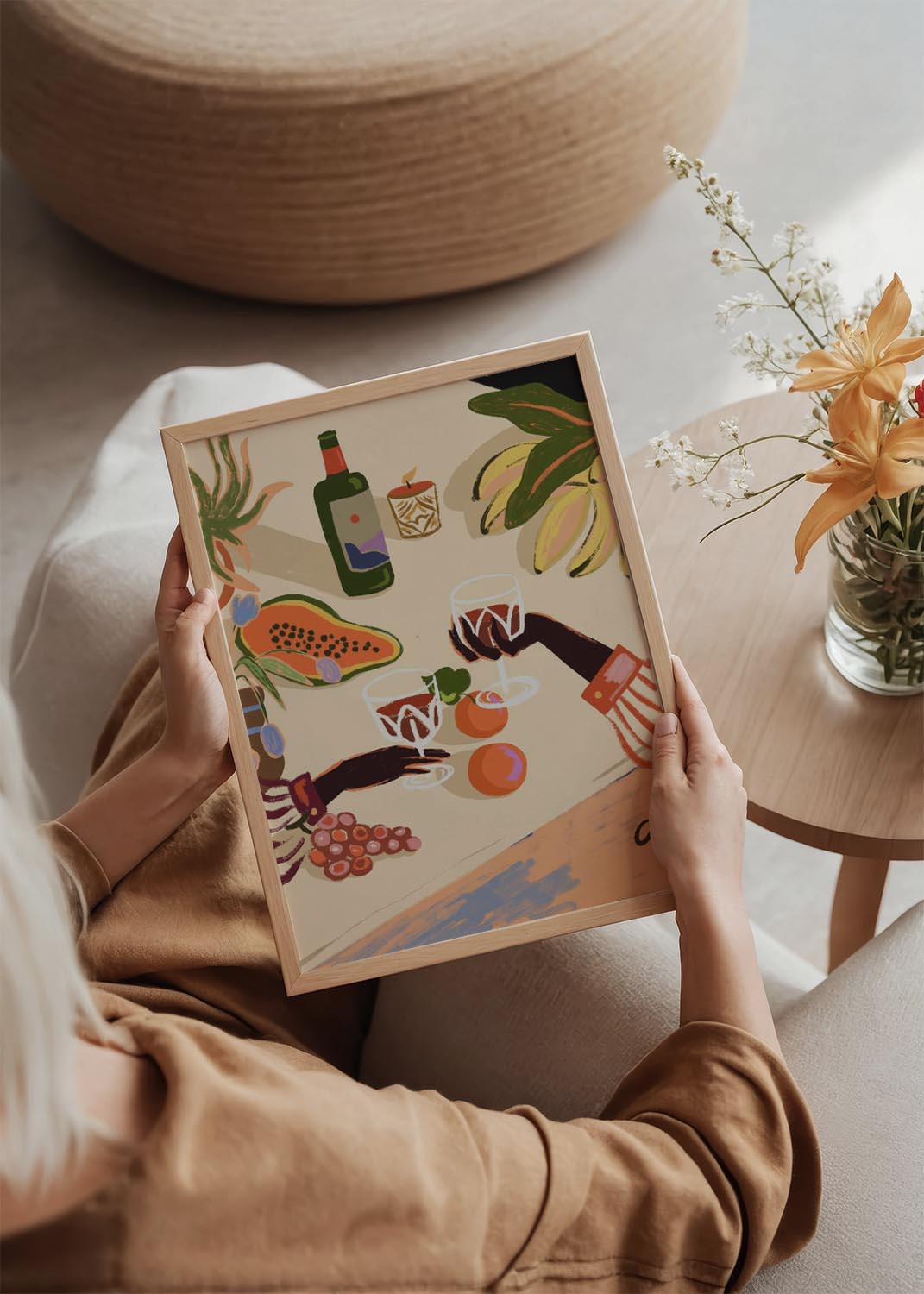 Illustration "Cheers to You" by Arty Guava, showing two hands toasting with red wine glasses over a table set with papaya, bananas, grapes, a wine bottle, and a lit candle.