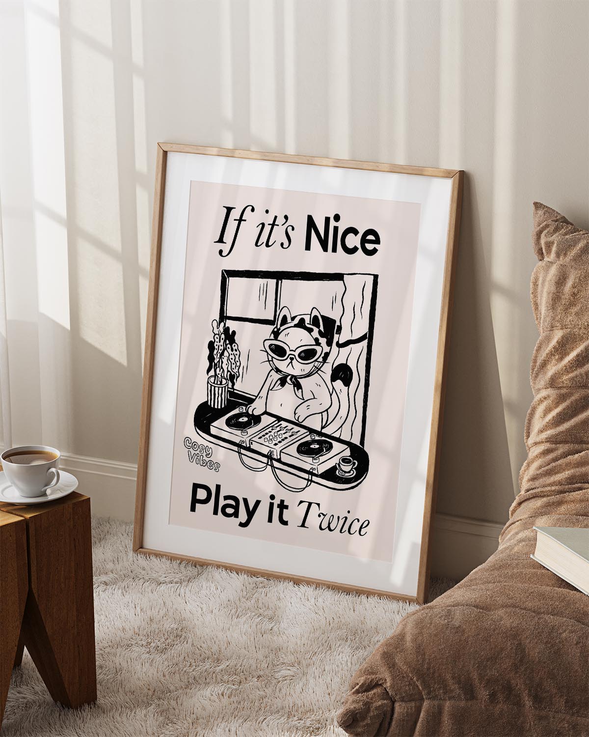 Illustrated poster of a cool cat DJ wearing sunglasses and a headscarf, spinning vinyl records on a turntable in front of a window. The text reads "If it’s Nice, Play it Twice" with "Cosy Vibes" written in the corner. The artwork is in a black-and-white, hand-drawn style.